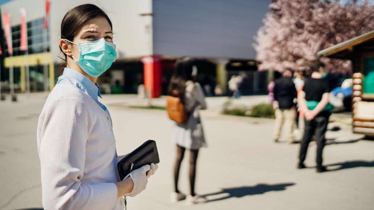 woman in facemask social distancing while waiting to enter a building