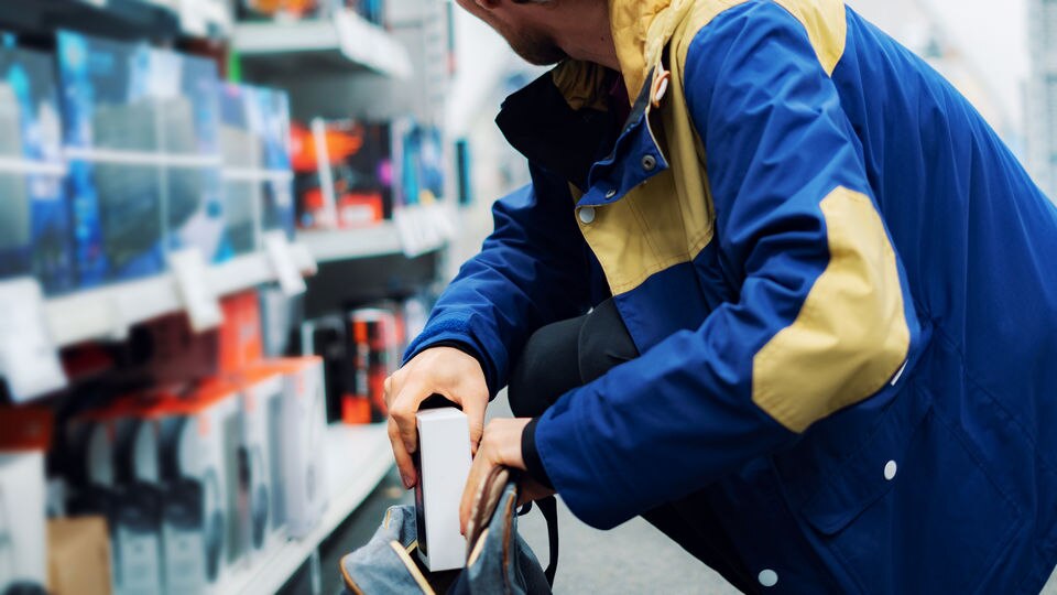 man in jacket crouching down and placing stolen item in his bag in retail store aisle