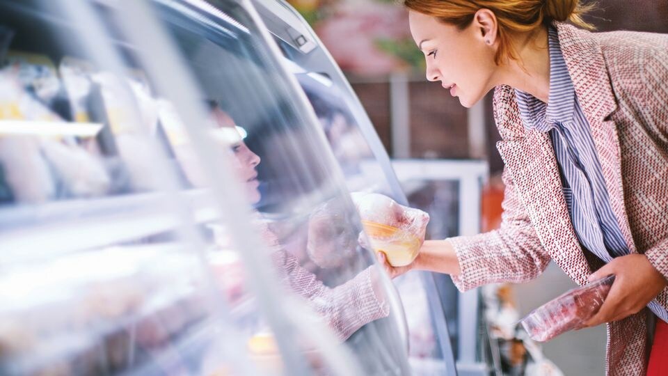 female shopper comparing products in retail grocery store refrigerated food case