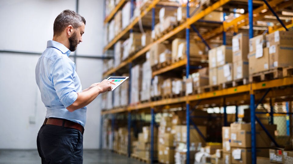 male retail store manager checking inventory in the warehouse reviewing data on his tablet device