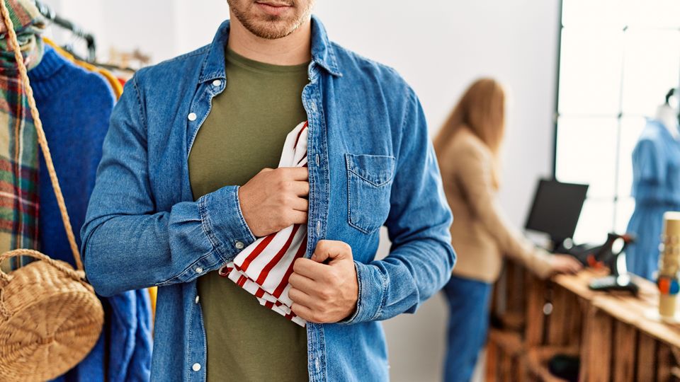 male shoplifter in a retail store facing the camera and sticking merchandise inside his jacket