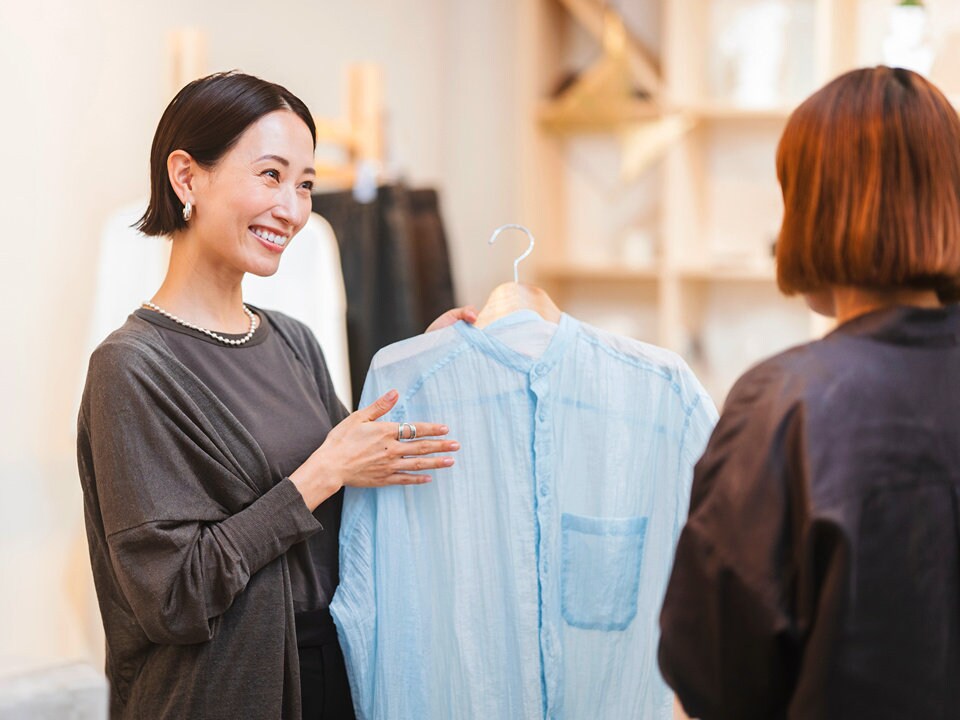 female retail clerk showing shirt to a female shopper in a bright modern retail apparel store