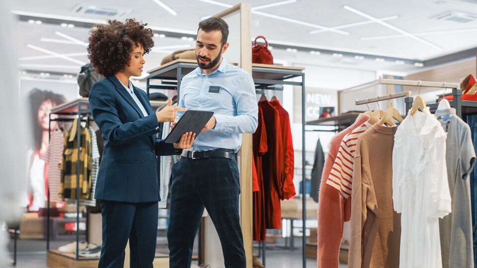 male and female retail store employees in an apparel store discussing inventory and sales data displayed on the female associates electronic device