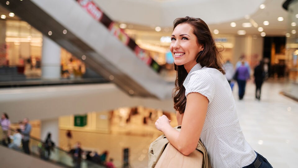 late 20s female shopper looking over an atrium and escalators in a multi-level indoor retail shopping mall
