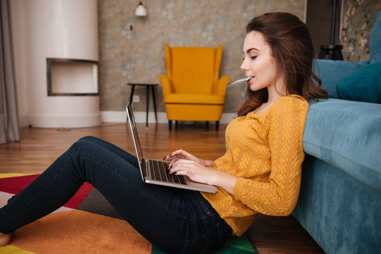 woman sitting on floor at home typing on laptop