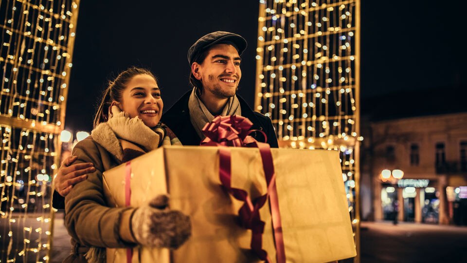 male female couple holding large gift box bought in holiday-decorated retail shopping area