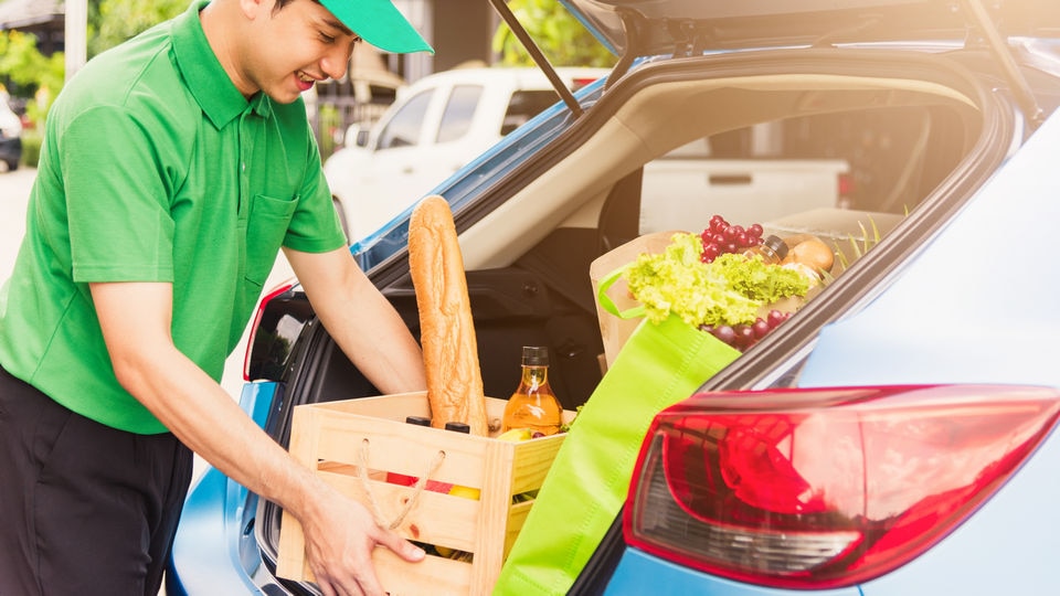 retail grocery worker loading wooden box of groceries into trunk of car