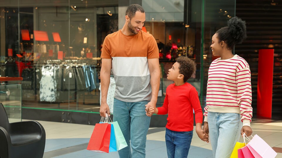 father mother and child shoppers leaving retail shopping center mall carrying purchases in brightly colored shopping bags