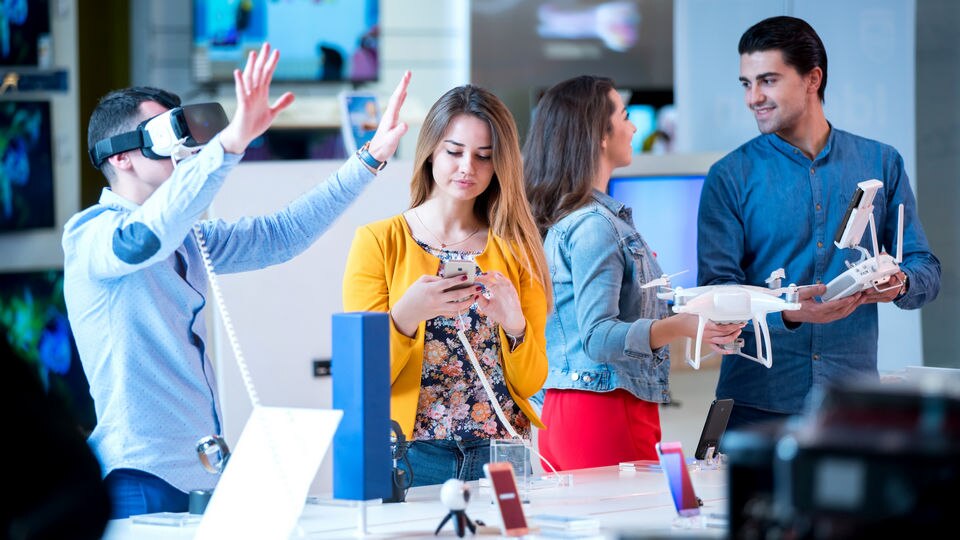 four millennials 2 male and 2 female shopping in retail electronics store looking at vr glasses and drones