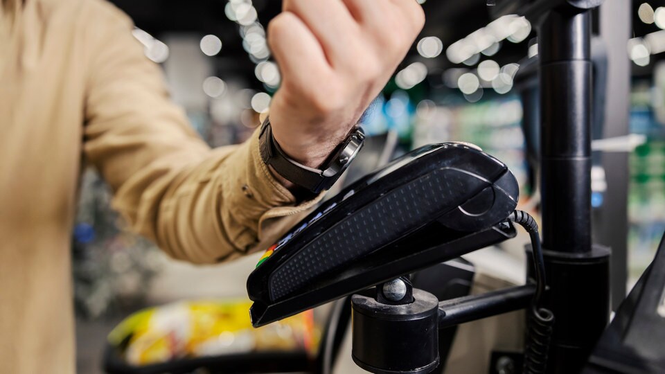 close up of a male shopper hand with smart watch paying bill at retail store on pos terminal