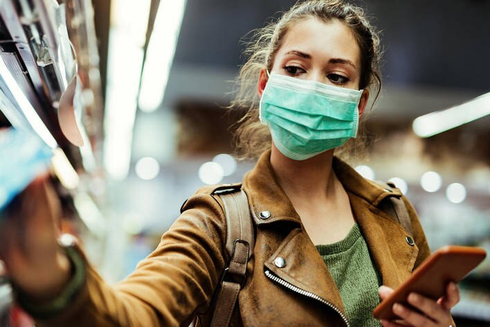 woman wearing mask looking at device while shopping