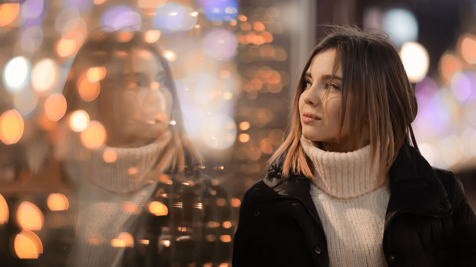 female shopper dressed in warm clothes looking at reflection in holiday decorated retail store window