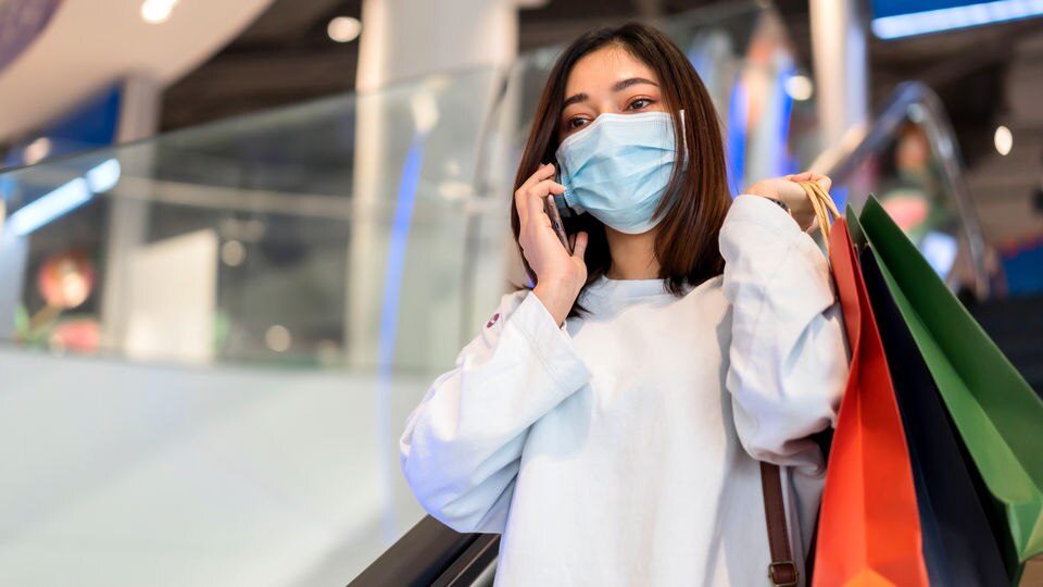 female shopper wearing mask with mobile phone in retail mall