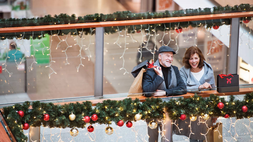 senior male female couple in holiday decorated retail mall carrying shopping bags