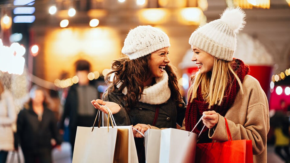 two female shoppers with shopping bags in christmas decorated retail shopping mall outside stores