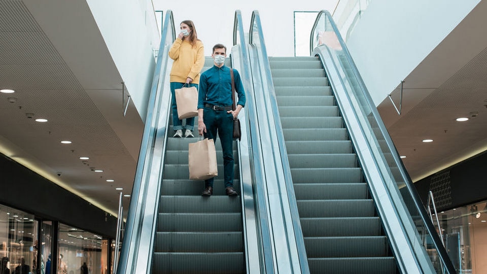 couple wearing masks descending escalator in shopping mall