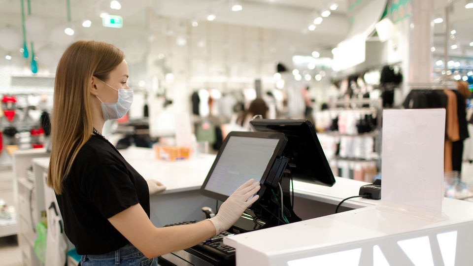 female store associate wearing mask stands at checkout counter screen in retail store