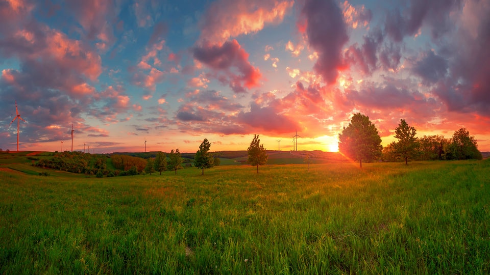 sunset over rural home with large fields of grass and scattered trees around the house with the sky a deepening blue and rose orange and gold tints to the clouds