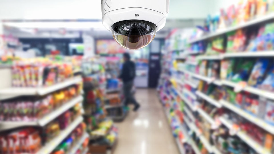video camera in retail grocery aisle with blurred customer and shelves in the background