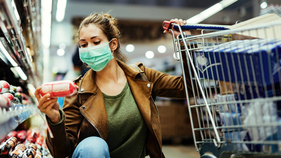 masked female shopper examining refrigerated product in retail grocery store