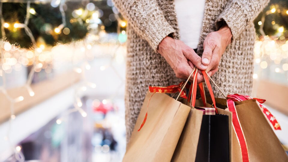 female shopper hands holding several retail shopping bags in holiday decorated shopping mall