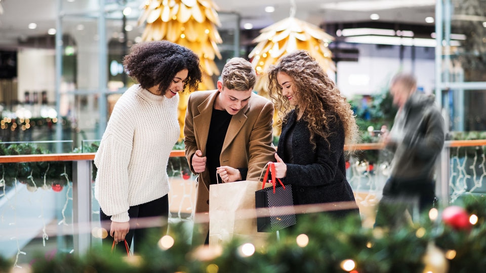 one male and two female friends in holiday decorated shopping mall looking at retail purchases in shopping bags