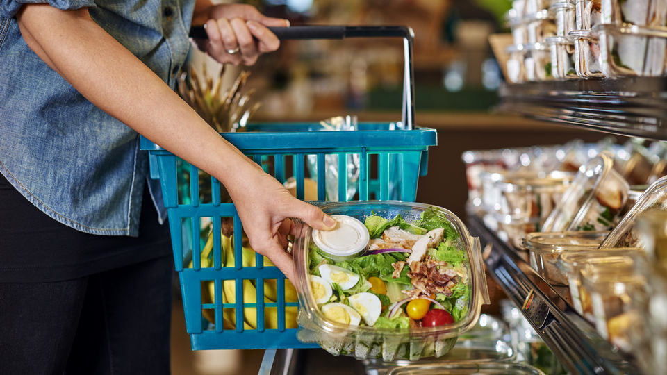 female grocery shopper putting fresh prepared salad in her shopping basket