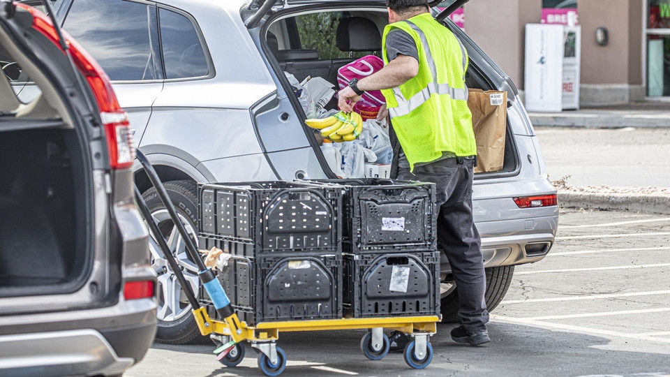 employee in a safety vest putting groceries into a customer vehicle