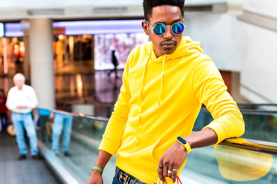 stylish man in yellow hoodie and sunglasses carring shopping bags on escalator inside retail shopping mall