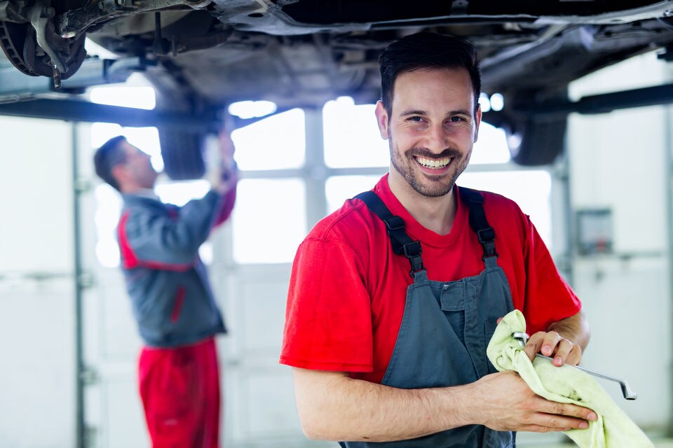 smiling uniformed auto mechanic on the work floor of a retail automobile repair and maintenance shop