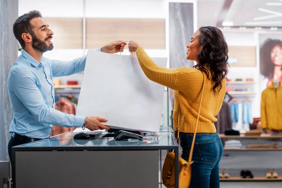 male retail store clerk hands shopping bag over register pos counter to female shopper