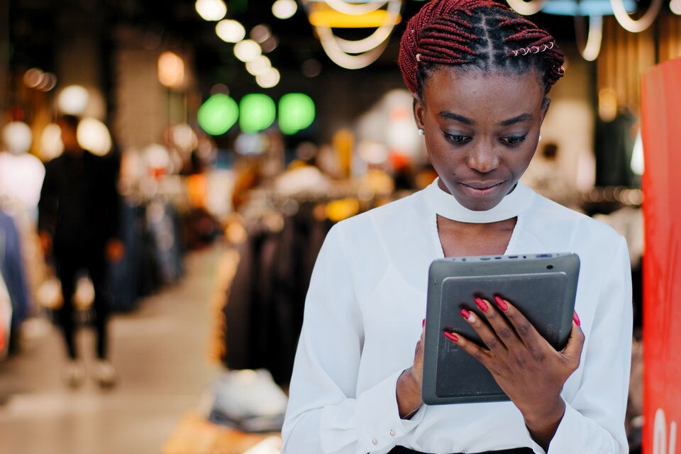 female retail store manager reviews store data on a tablet device while standing at shopping mall store entrance