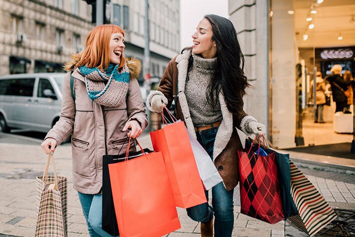 two female shoppers carrying shopping bags outside retail store