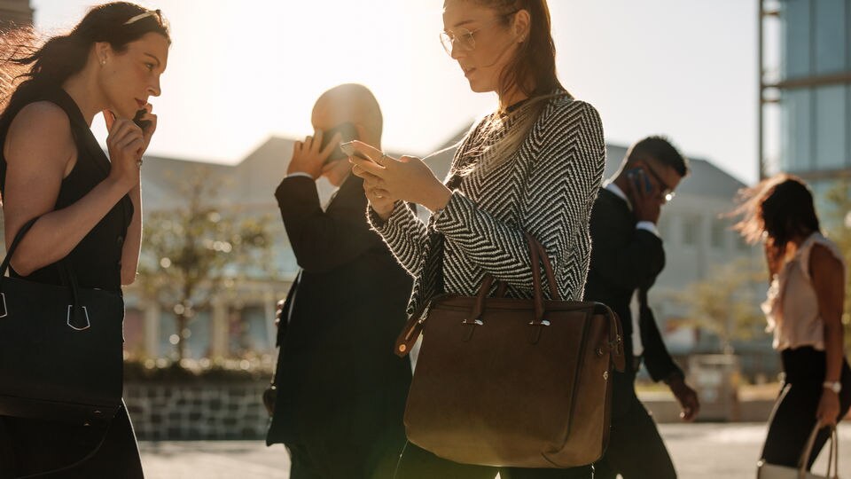 five business people walking in various directions each talking on cellphone in office areas with mountains in background