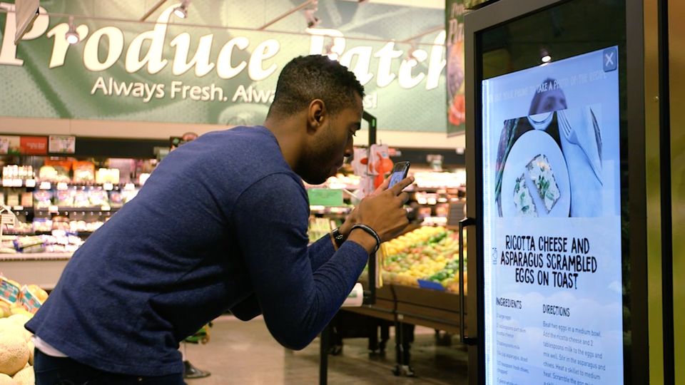 man in retail store taking photo with device of video display data