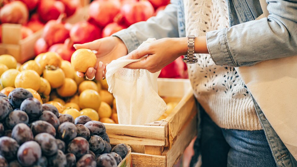 female hands choosing lemons from a produce display in a retail grocery store and putting them in an eco-friendly bag
