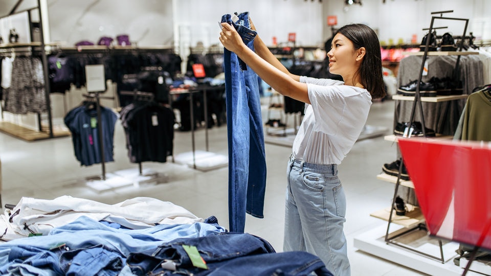 young asian female shopper looking at a pair of jeans in a retail unisex apparel store