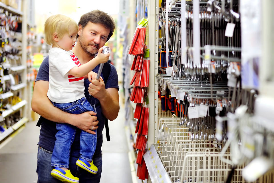 male shopper holding child and looking at tool display in retail hardware diy store