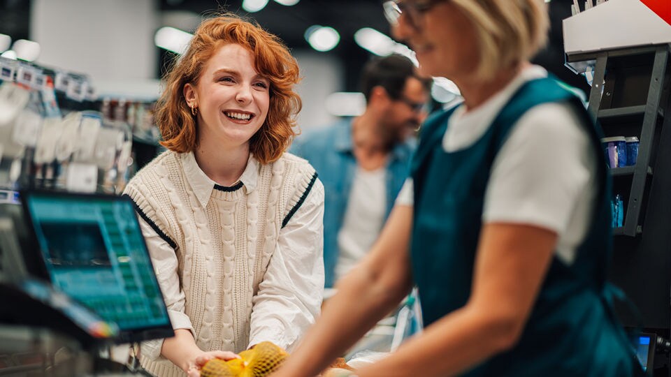 smiling young female shopper checking out her purchases with the cashier at the counter of a retail grocery store