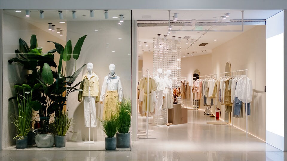 retail apparel store mall entrance with plants and mannequins in the shop window