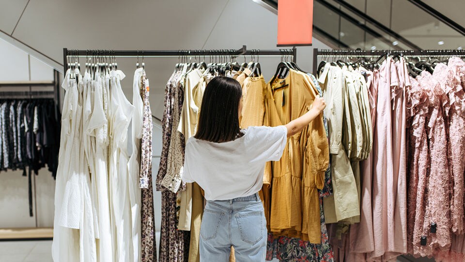 young female shopper looking at dresses and blouses on a rack in a retail apparel store