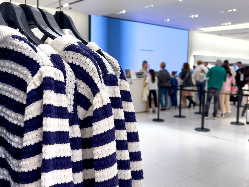 busy retail apparel store with sweaters on a rack in the foreground and several queues of shopper at register in background