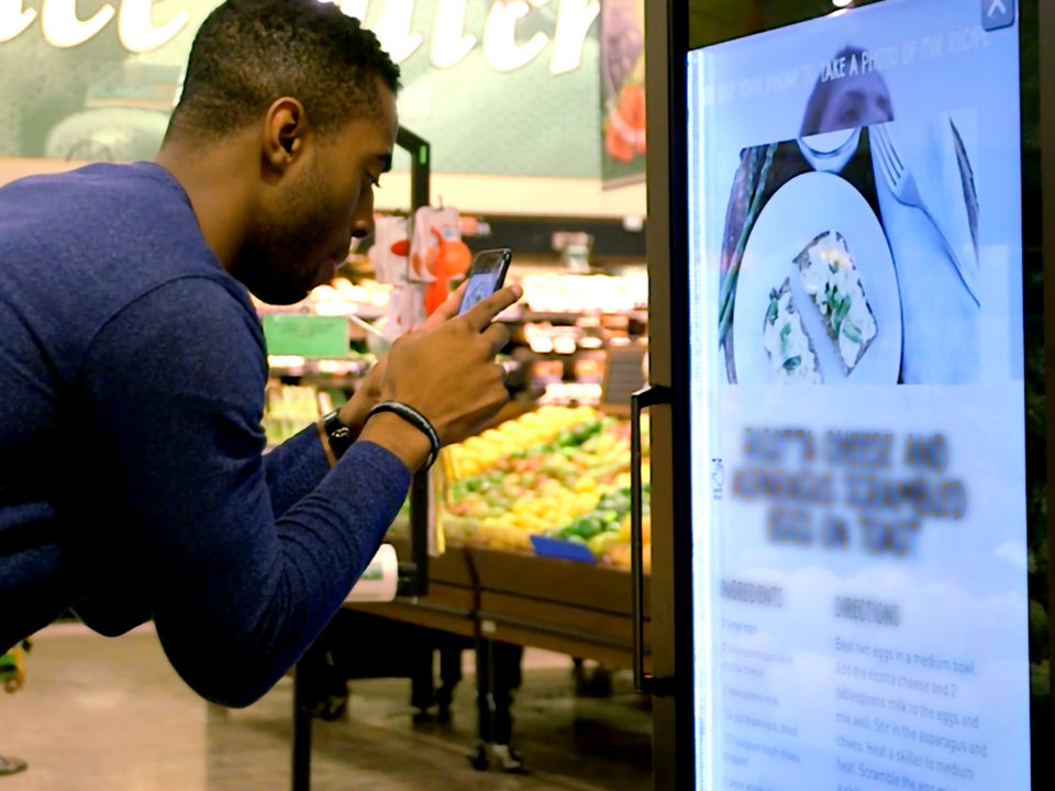retail shopper using phone to interact with in-store video display in retail grocery store