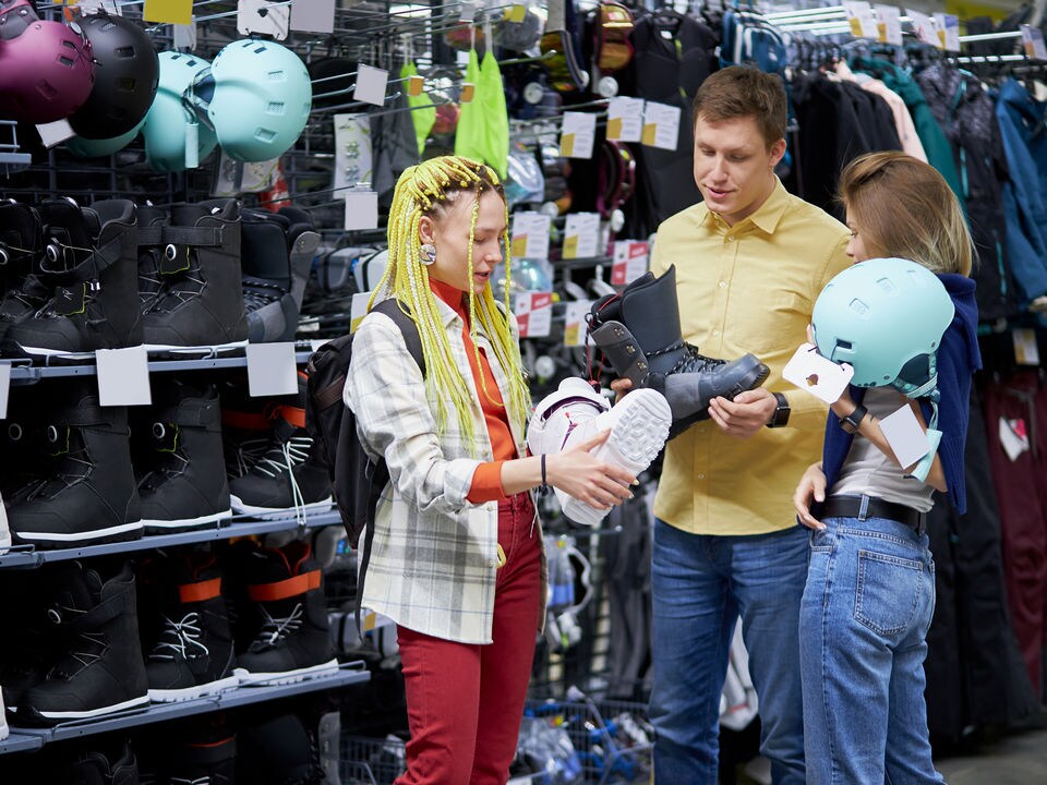 male retail sporting goods store clerk showing ski boots to two young female shoppers
