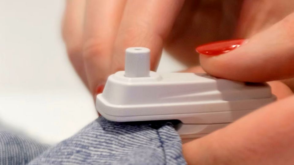 woman retail store associates hand with red nailpolish placing a sensormatic infuzion hard tag on the hem of a pair of jeans