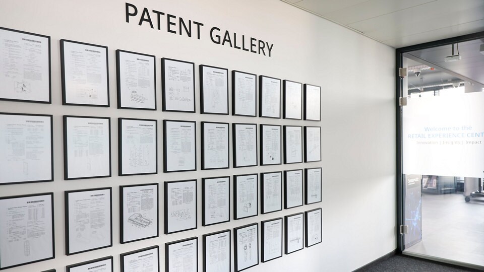 Wall display labeled “PATENT GALLERY” featuring dozens of framed patent documents arranged in a grid.