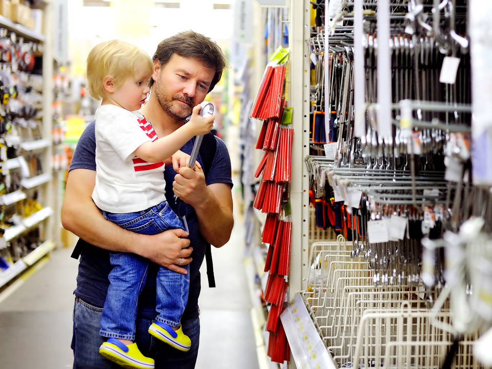 male shopper holding child and looking at tool display in retail hardware diy store
