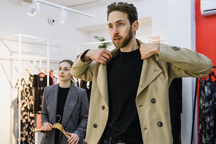 man trying on coat while female store associate watches