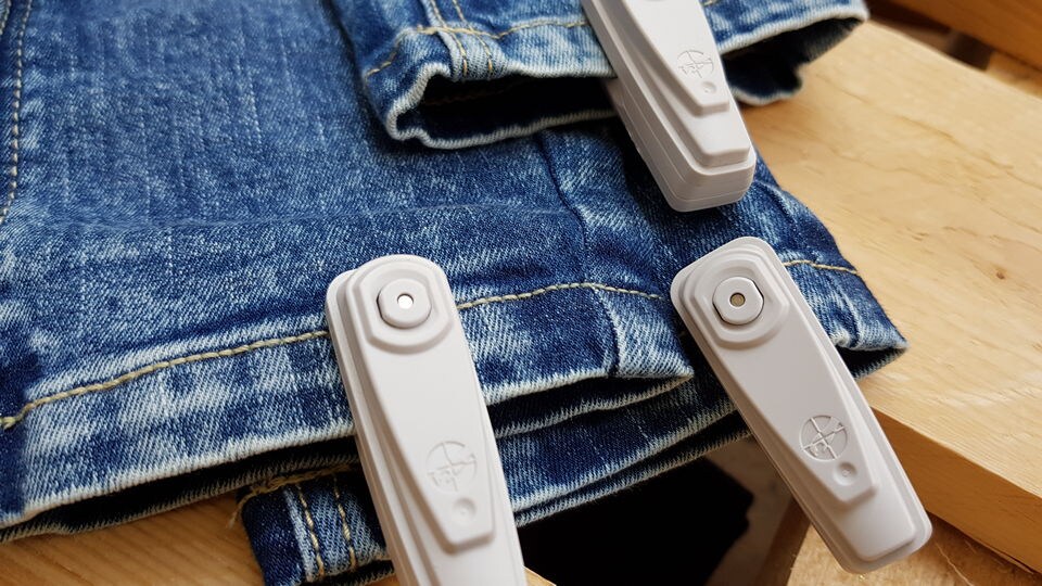 close up of a pile of several pair of denim jeans with sensormatic merchandise protection hard tags attached
