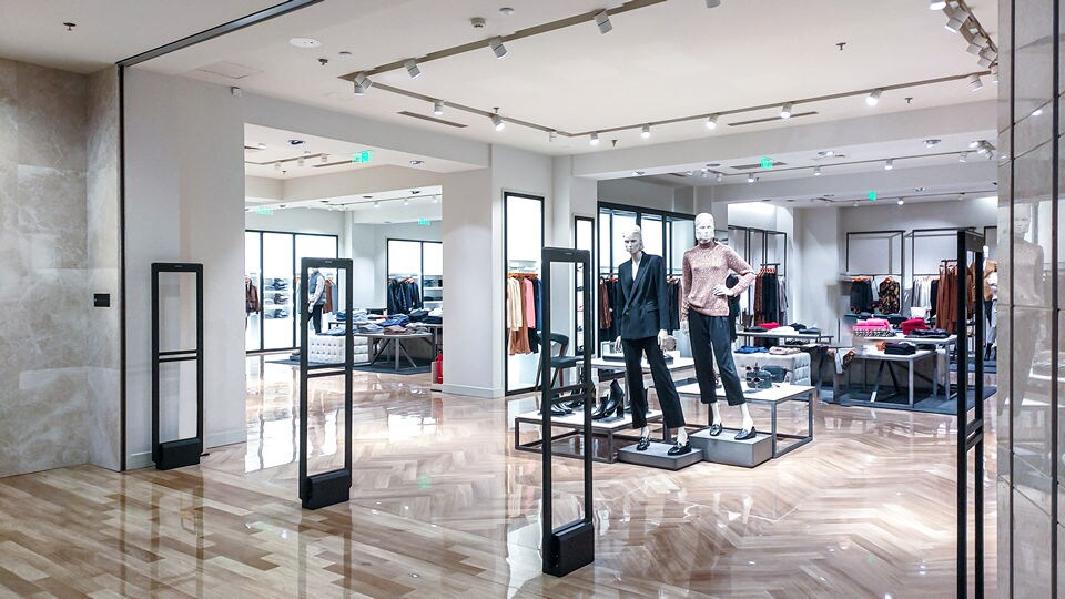 entrance to a well-lit upscale mall retail apparel store with two mannequins in midground and sensormatic eas pedestals in foreground